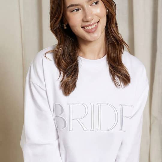 Smiling bride-to-be wearing the white BRIDE Sweatshirt with tonal embroidered lettering